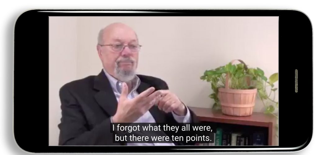 There is an older white man who wears glasses shown in a video on an iPhone. He is dressed in formal suit, and signing in ASL. The caption shows in white on a translucent black background: "I forgot what they all were, but there were ten points."