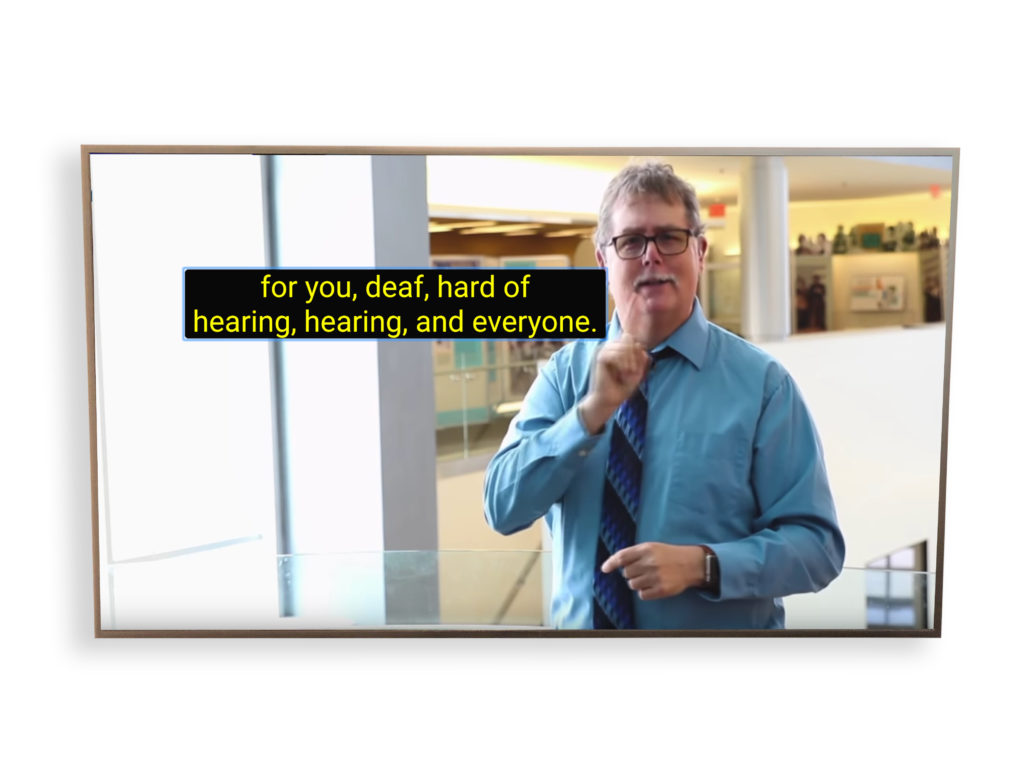 On a HD TV, a white man who wears black-rimmed spectacles is in the Sorenson Language and Communication Center.  He is dressed in a blue shirt and wears a striped tie. He is facing the camera and signs in ASL. The caption is positioned next to his face and shows "for you, deaf, hard of hearing, hearing, and everyone."